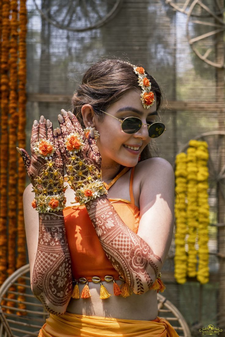 a woman in an orange outfit holding her hands up to show the hendi design