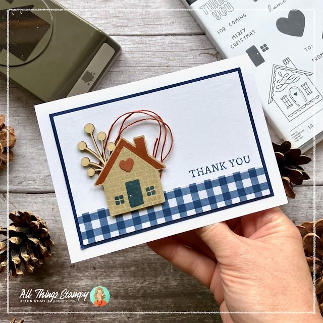 a hand holding up a card with a house on it and pine cones around it