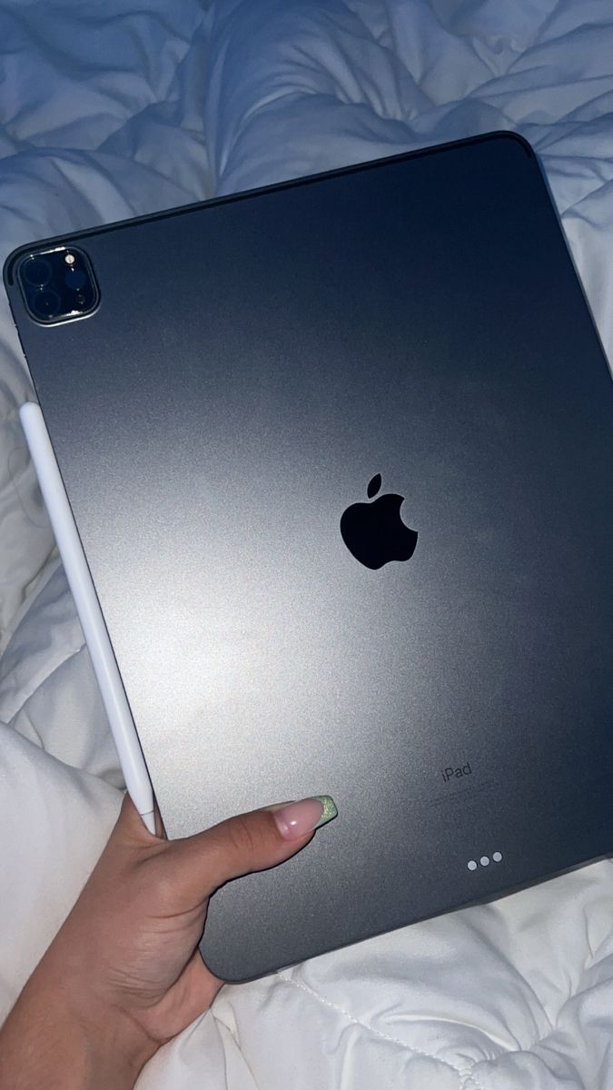 a person's hand holding an apple ipad on top of a white bed sheet