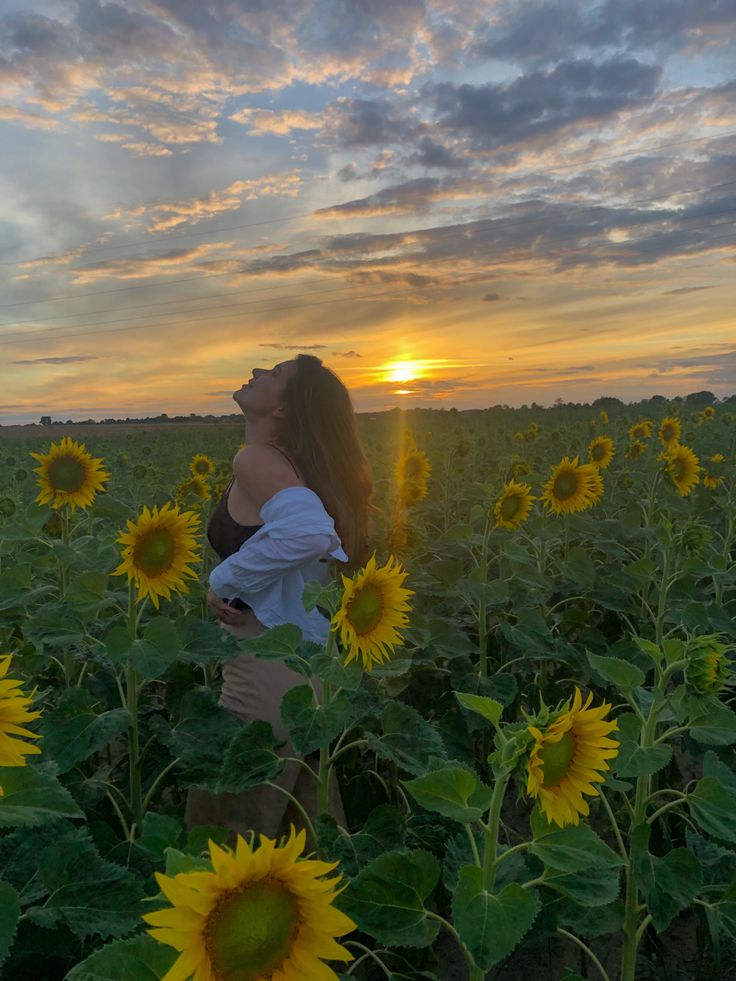 a woman standing in the middle of a field of sunflowers at sunset or dawn