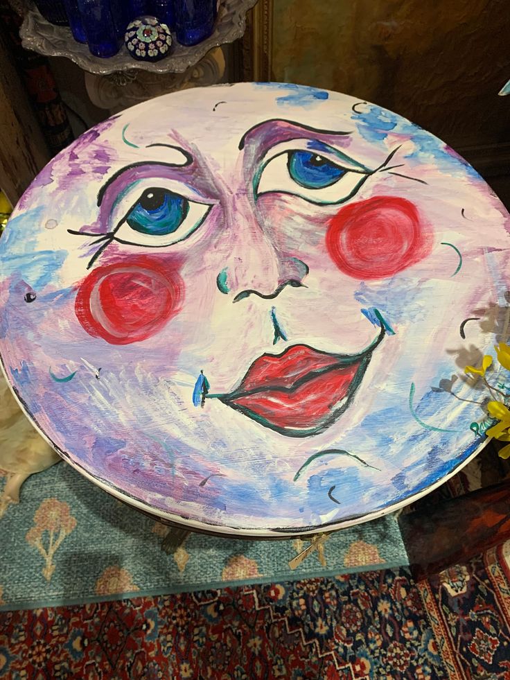 a plate with a face painted on it sitting on a table next to flowers and vases