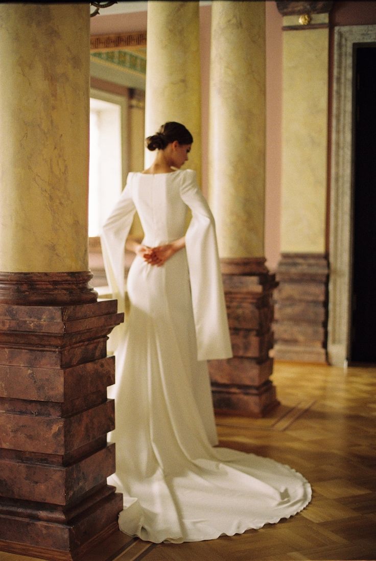 a woman in a white dress standing next to columns and pillars with her hands on her hips