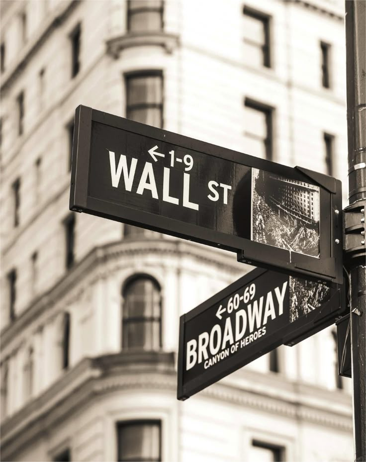 two street signs on the corner of wall st and broadway in front of a building