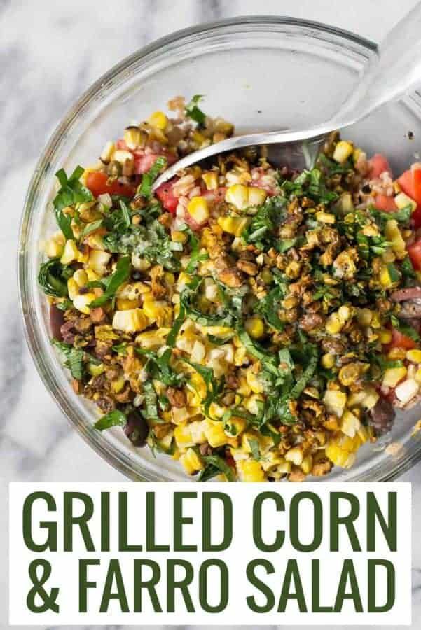 grilled corn and faro salad in a glass bowl with a spoon on the side