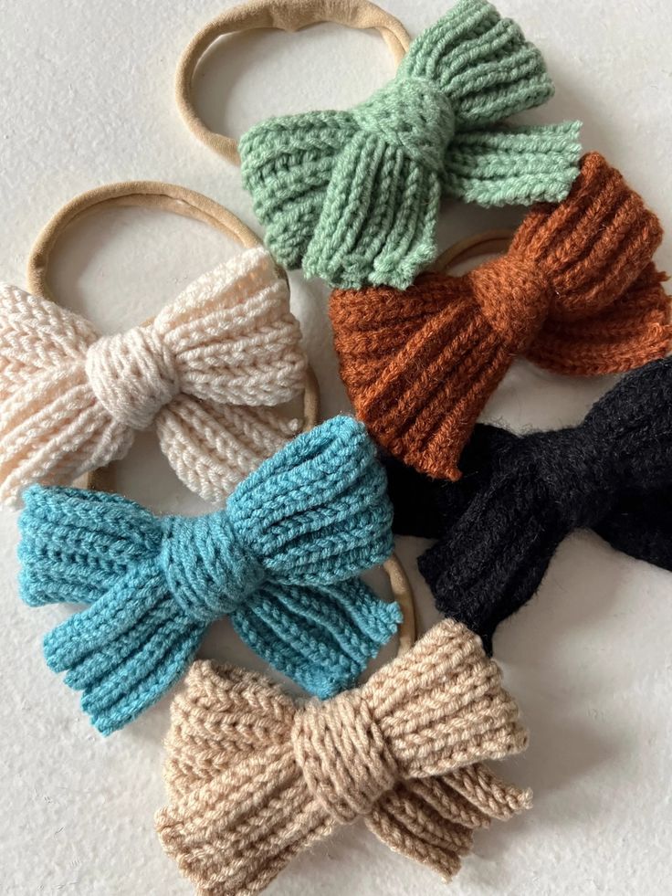 four knitted bows are shown in different colors and sizes, all tied together to each other