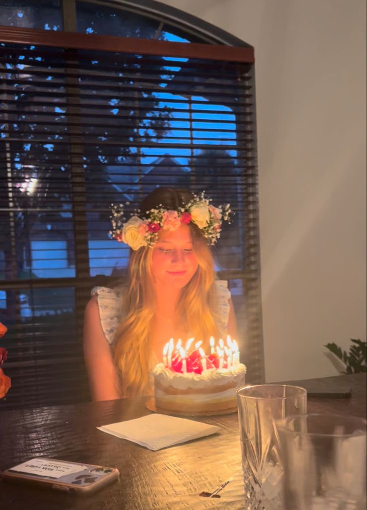 a woman sitting in front of a birthday cake with lit candles on top of it