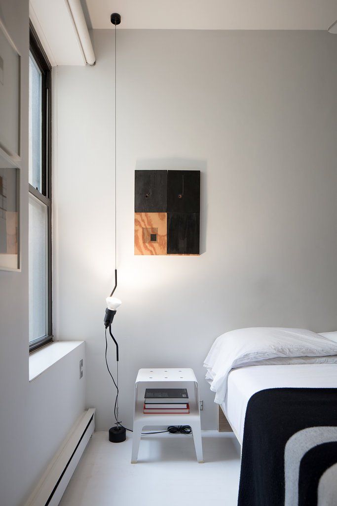 a bedroom with a bed, nightstand and lamp on the wall next to it's window