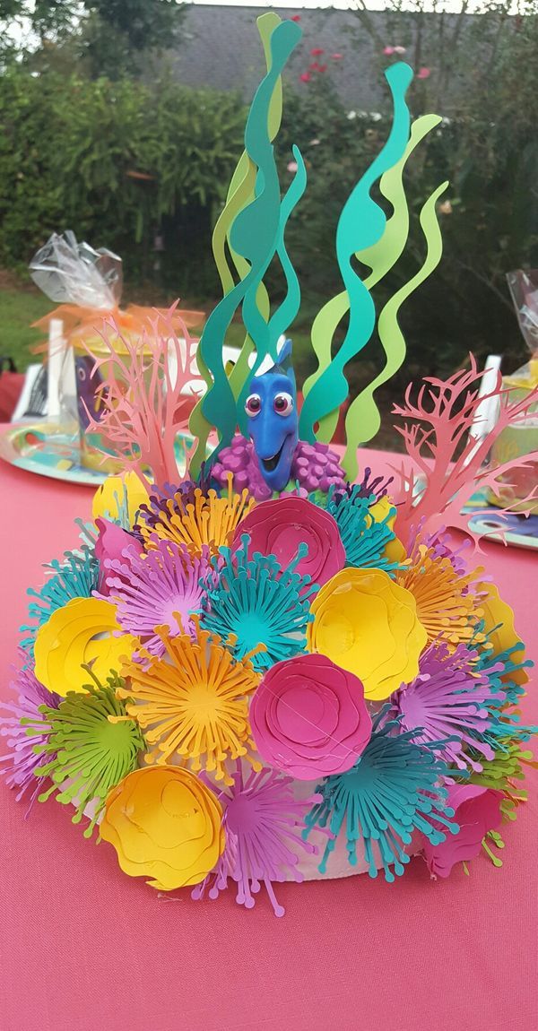 a colorful centerpiece with paper flowers and sea creatures on it's head is sitting on a pink table cloth