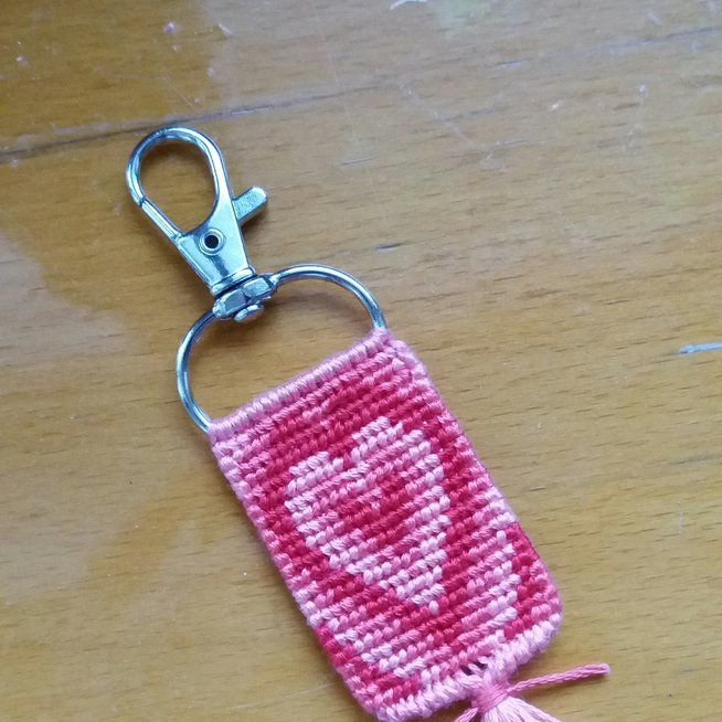 a crocheted key chain with a pink and white heart on it, hanging from a metal hook