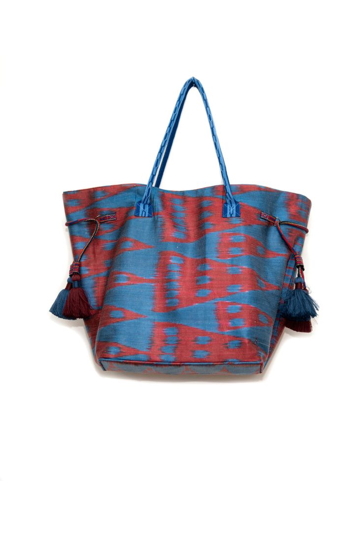 Ikat bag made with hand-woven silk ikat fabric. The side tassels help adjust the upper width of the bag. You can pull the tassels to make the bag look narrower or let it out to make it wider. The lining is made of traditional hand-made striped bekasam fabric. Inner pockets, one with zipper. Snap magnetic closure. Handles are made of hand-woven bands. This bag is a unique addition to your outfit. Match it with our ikat kaftans or contemporary outfits. Upper Width: 50cm (20”) Lower Width: 30cm (12 Woven Travel Tote Bag, Travel Tassel Shoulder Tote Bag, Travel Tote Shoulder Bag With Tassels, Travel Tote Bag With Weaving Work, Blue Tassel Bags For Daily Use, Blue Bag With Tassels For Everyday Use, Blue Everyday Bag With Tassels, Blue Shoulder Bag With Tassels For Daily Use, Traditional Fringe Bag