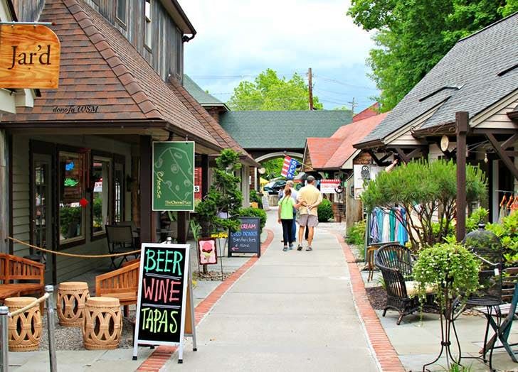 two people walking down a sidewalk in front of small shops with signs on the sidewalks