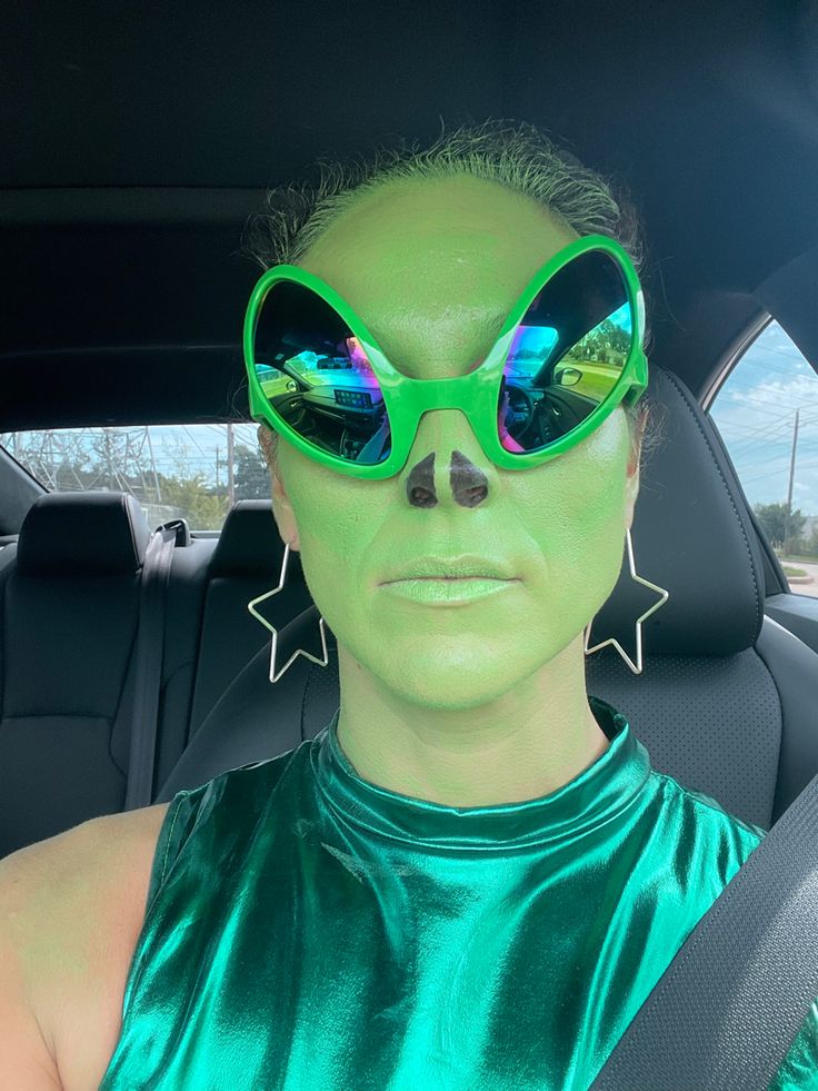 a woman with green makeup and sunglasses in the back seat of a car looking at the camera