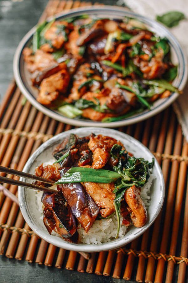 two plates filled with meat and vegetables on top of a bamboo mat next to chopsticks