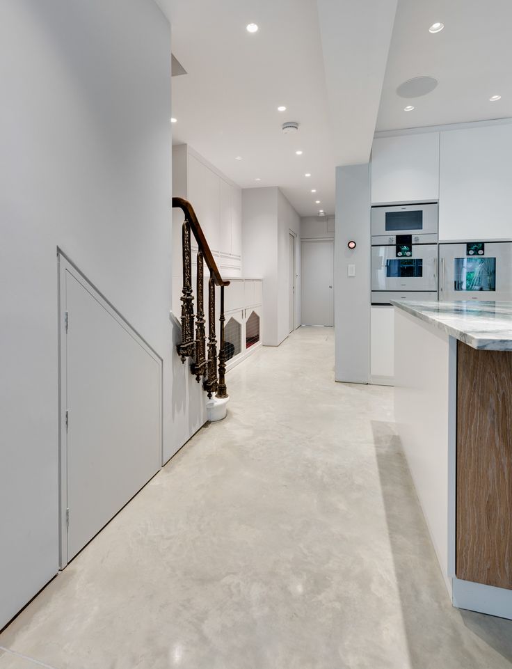 an empty white kitchen with stairs leading to the upper floor and another room in the background