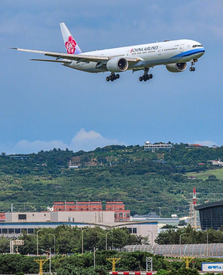 an airplane is flying low to the ground in front of some trees and buildings on a hill