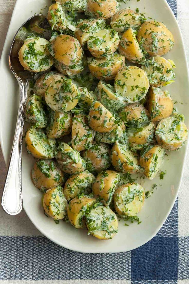 a white plate topped with potatoes covered in pesto and parsley next to a fork