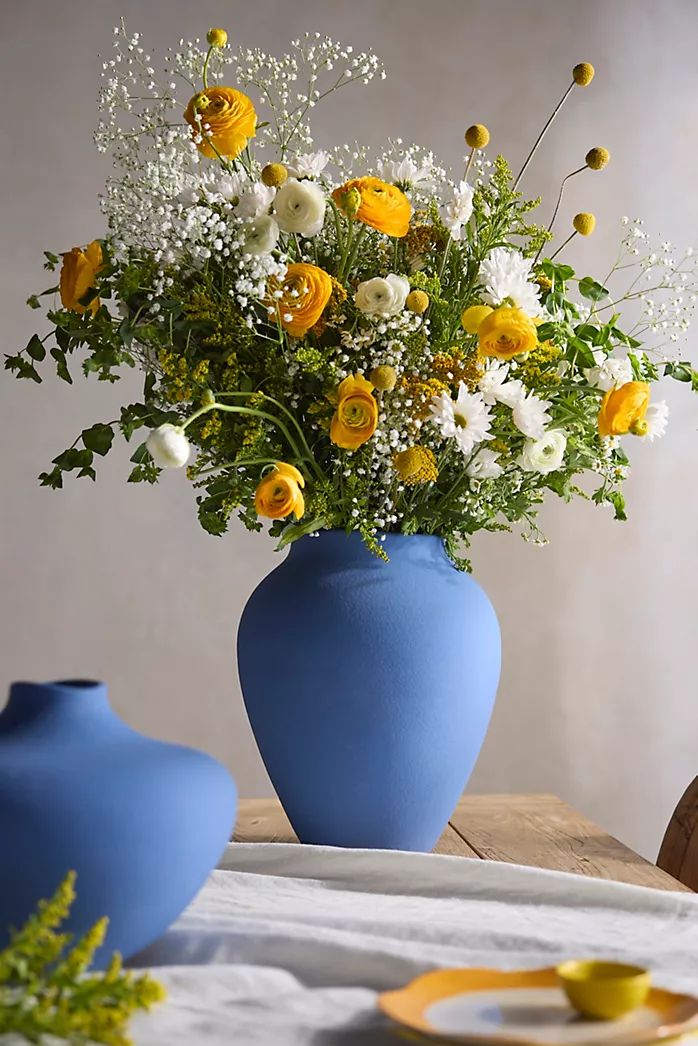 two blue vases with yellow and white flowers in them sitting on a wooden table