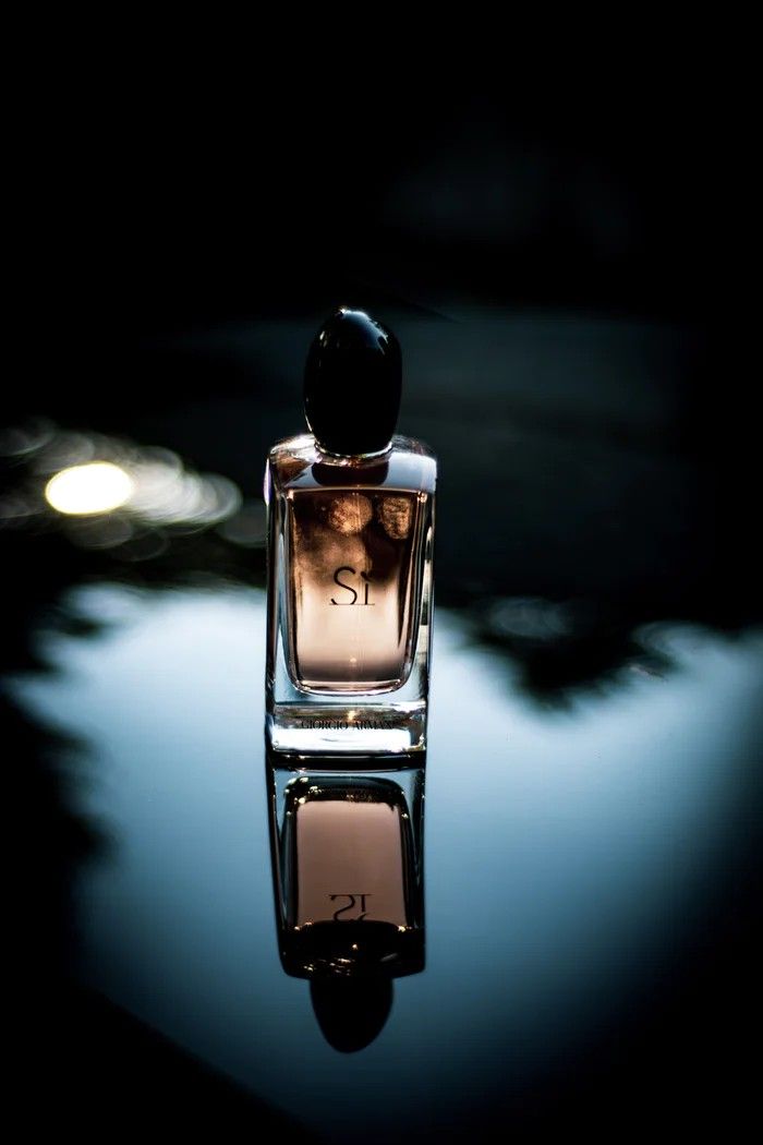 a bottle of perfume sitting on top of a table next to a light reflecting in the water