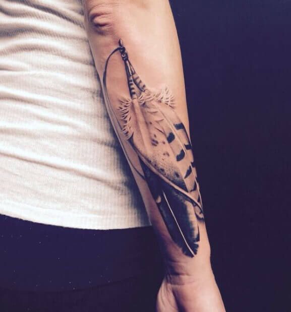 a person with a black and white tattoo on their arm holding an arrow in the shape of a feather