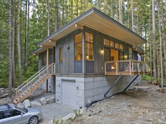 a small cabin in the woods with stairs leading up to it's second floor