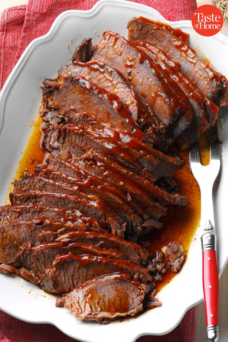 a plate with sliced meat and sauce on it next to a red napkin, fork and knife