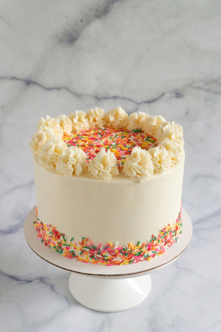 a cake with sprinkles and white frosting on a marble table top