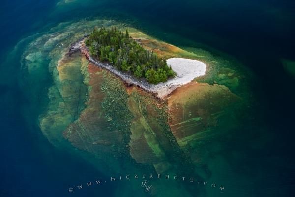 an island in the middle of some water with trees on it's shore and blue sky above