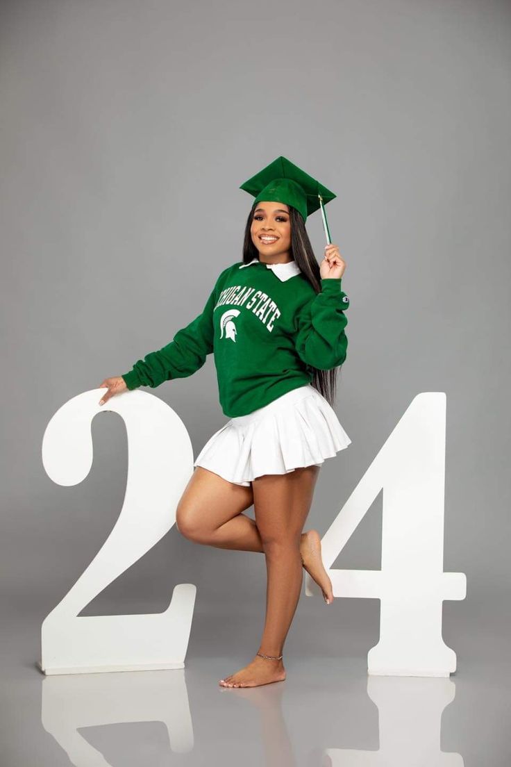 a woman in a green sweatshirt and white skirt posing for the camera with her graduation cap on