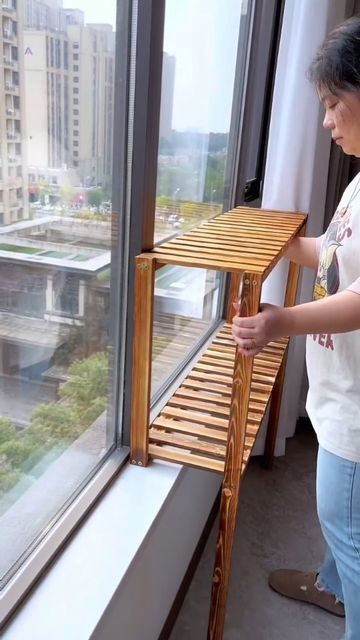 a woman standing next to a window with a wooden shelf on it's side