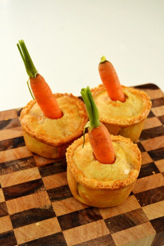 three small pies with carrots sticking out of them on a wooden cutting board