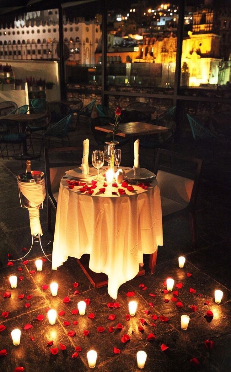 a table with candles and rose petals on it in the middle of a courtyard at night