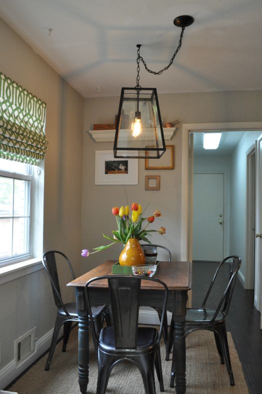 a dining room table with four chairs and a vase on top of it, in front of a window