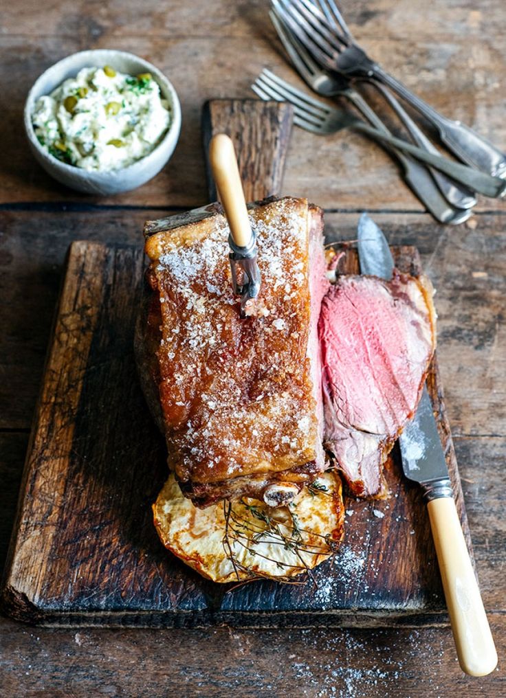 a piece of meat sitting on top of a wooden cutting board next to a knife and fork