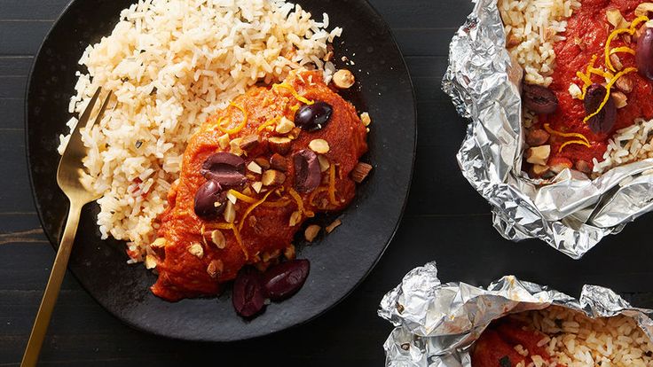 two black plates filled with food on top of a wooden table next to silver foil