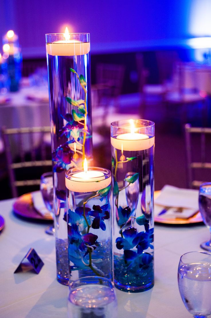 two tall vases filled with blue flowers and lit candles