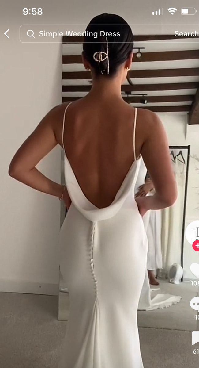 the back of a woman's wedding dress in front of a mirror with her hand on her hip