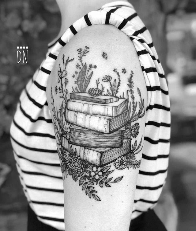 a woman's arm with books and flowers tattoo on her left shoulder, while she is wearing a striped shirt