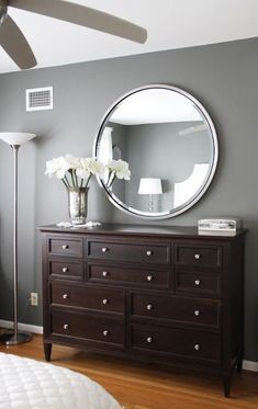 a bedroom with a bed, dresser and large round mirror on the wall above it