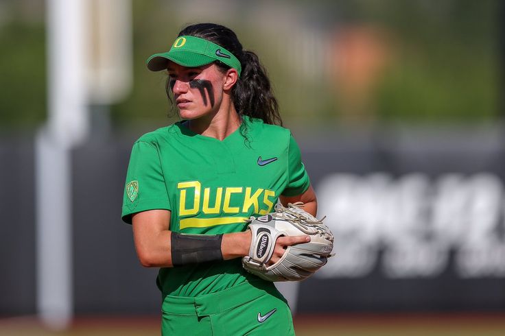 a female baseball player wearing a green uniform and holding a catchers mitt in her hands