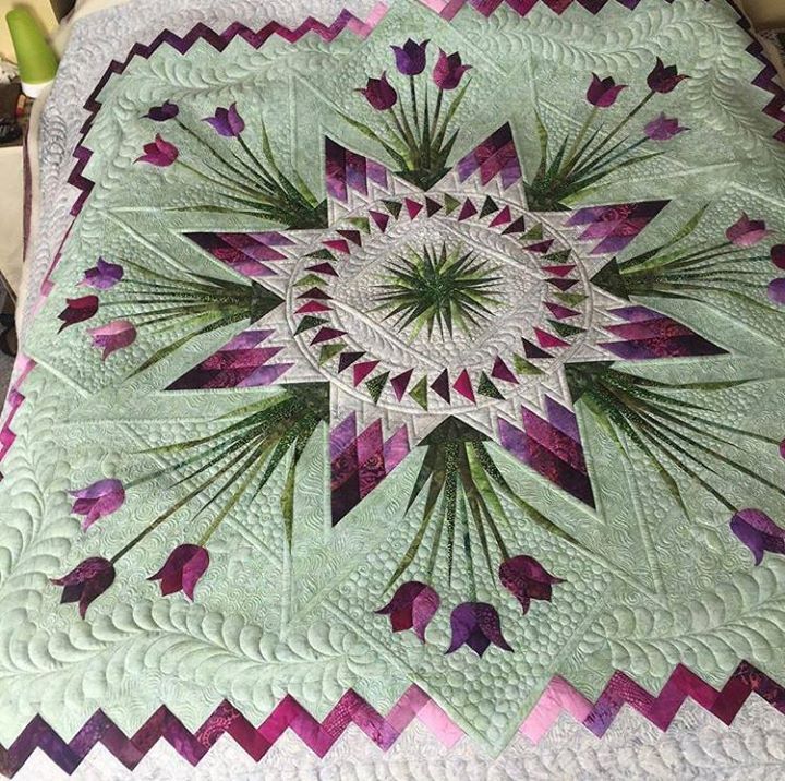 a green and purple quilt on top of a bed with flowers in the center,