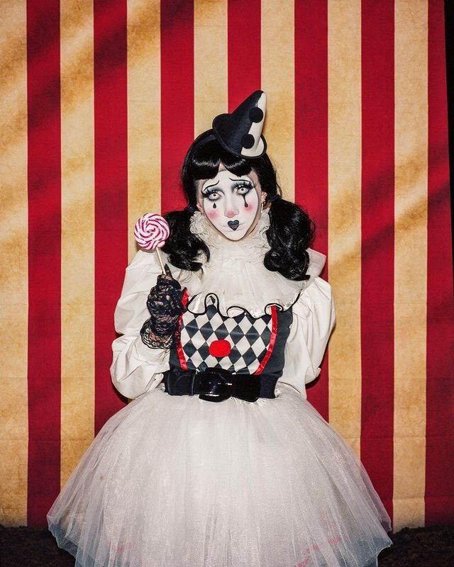 a woman dressed as a clown holding a lollipop in front of a striped wall