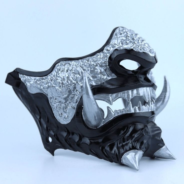 a black and silver mask with spikes on it's face is seen against a white background