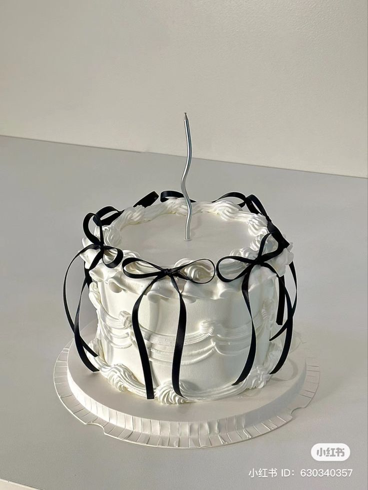 a white cake with black ribbons and a single candle on top is sitting on a plate