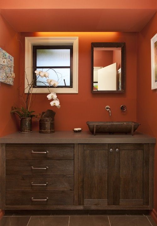 a bathroom with an orange wall and two sinks in the center, along with a mirror on the wall