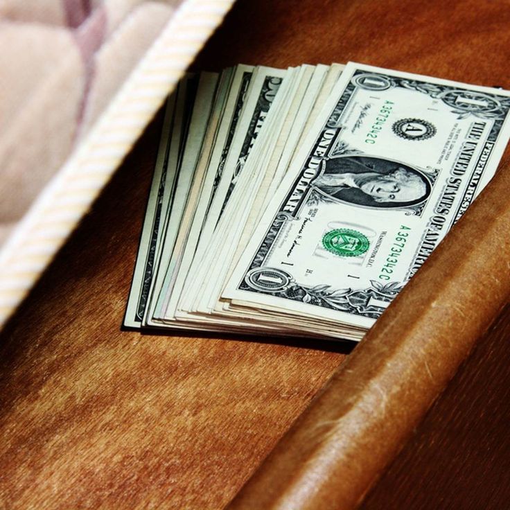 stack of money sitting on top of a wooden table next to a blanket and pillow