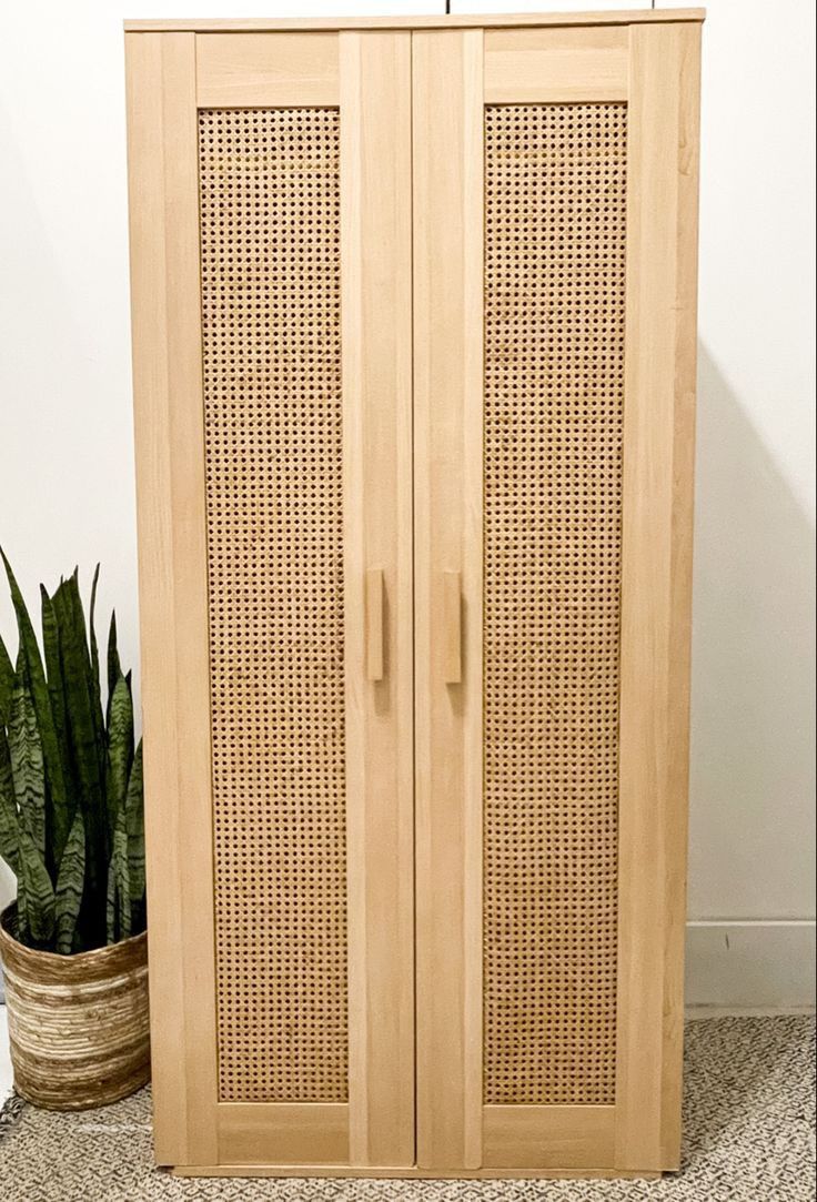 a tall wooden cabinet with wicker doors next to a potted plant on the floor