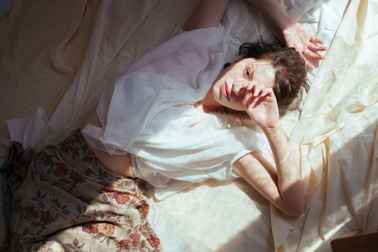 a woman laying on top of a bed in a white shirt and floral skirt with her hands behind her head