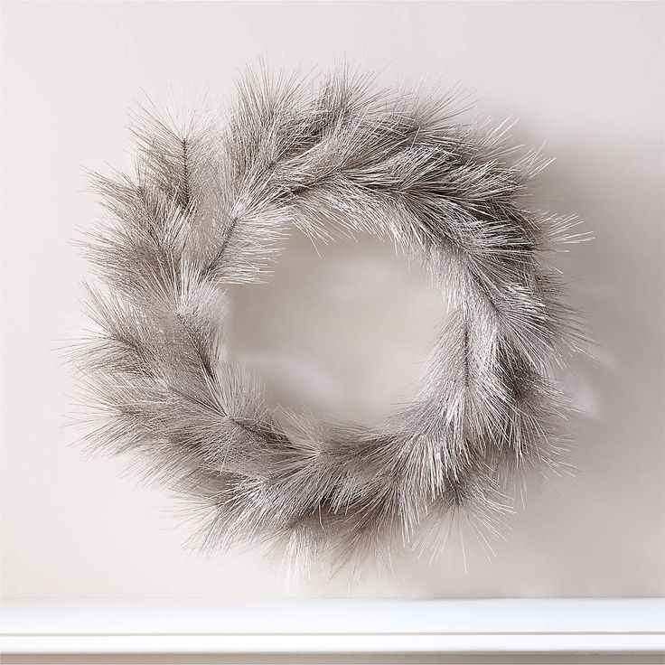 a white frame with a silver fur wreath hanging on it's side, in front of a wall