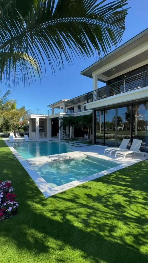 a large swimming pool in front of a house with grass and flowers on the lawn