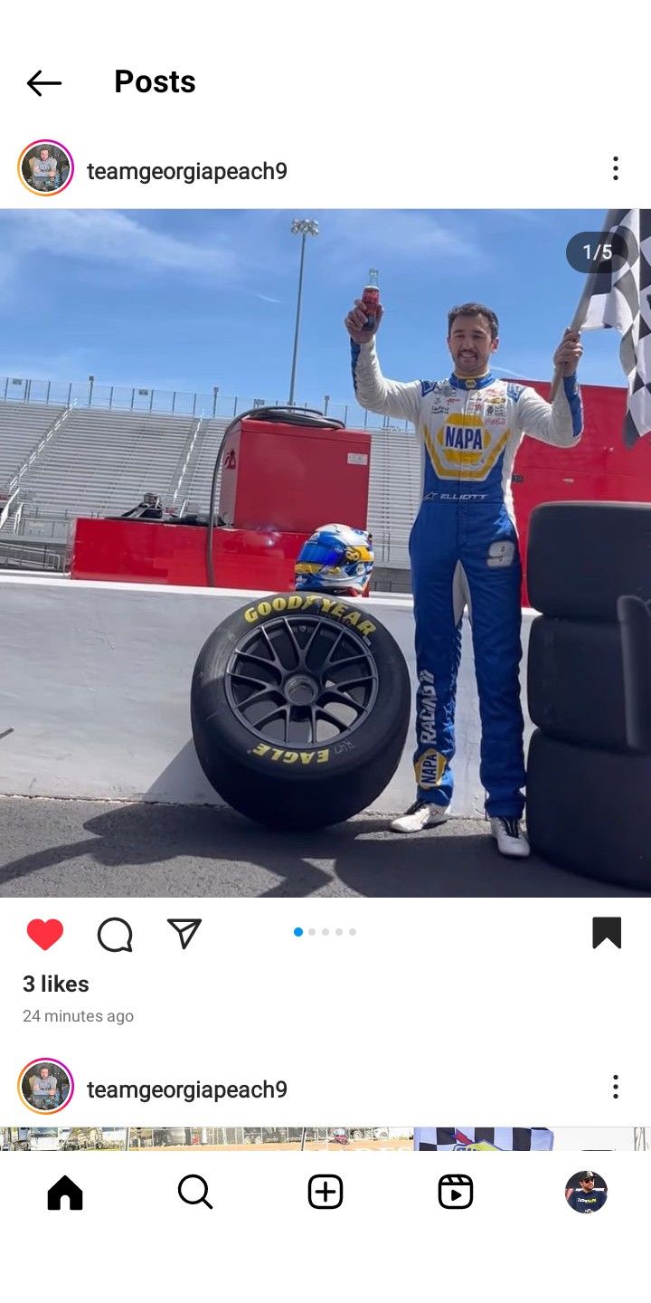 a man standing next to a tire on top of a race track with his arms in the air